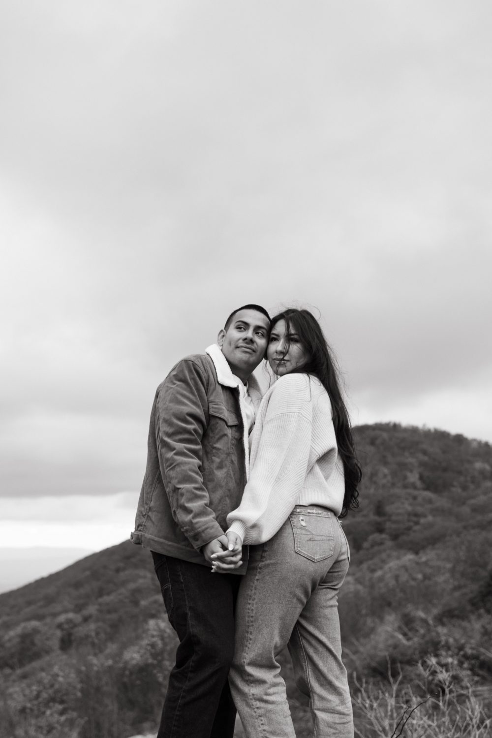 fall engagement session couple on mountainside looking into distance holding hands
