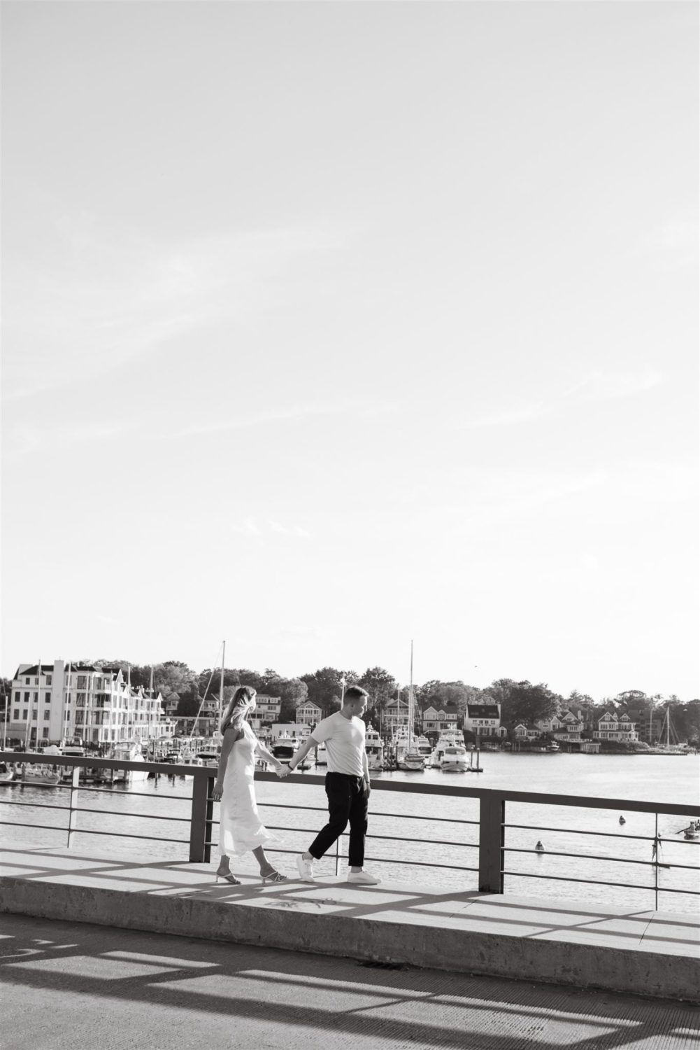 black and white annapolis marina engaged couple walking bride holding hands