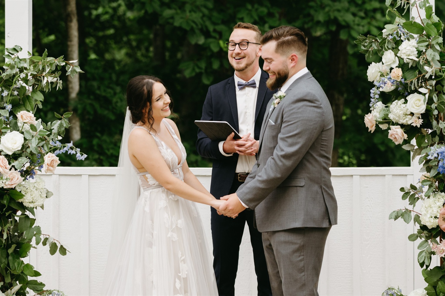 bride and groom smiling holding hands reading vows altar