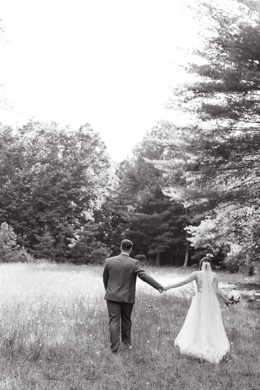 black and white portrait bride and groom holding hands walking through field