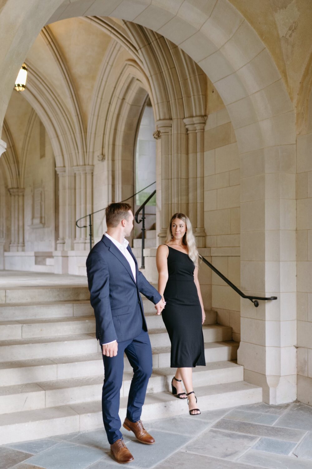 groom to be leading bride down stairs washington dc engagement session black dress navy suit
