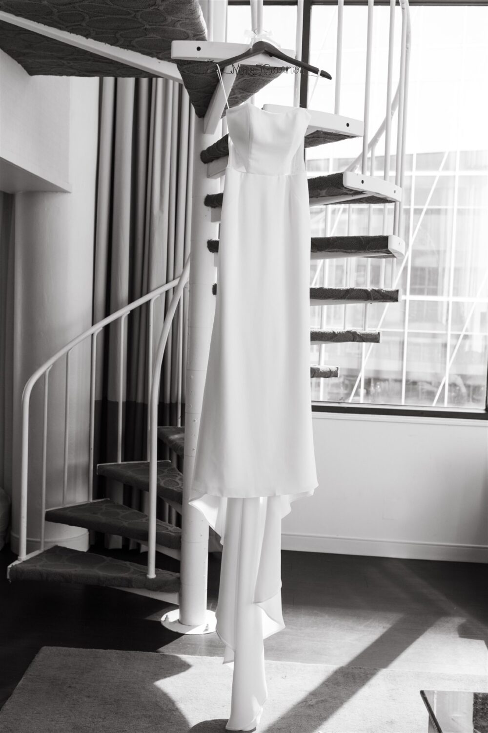 bridal gown hanging from custom hanger on spiral staircase modern wedding