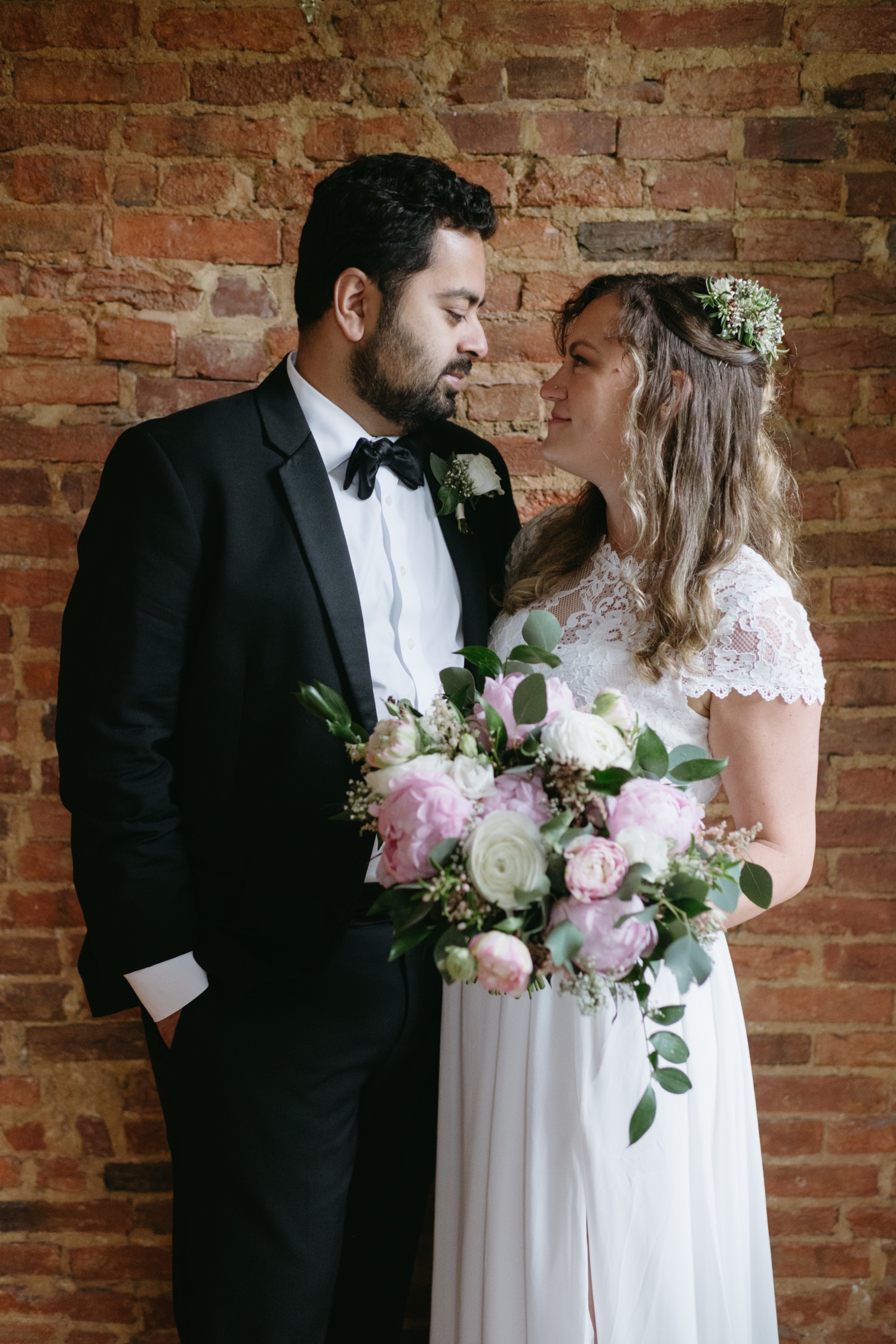 bride and groom looking into each others eyes brick backdrop pink and white florals