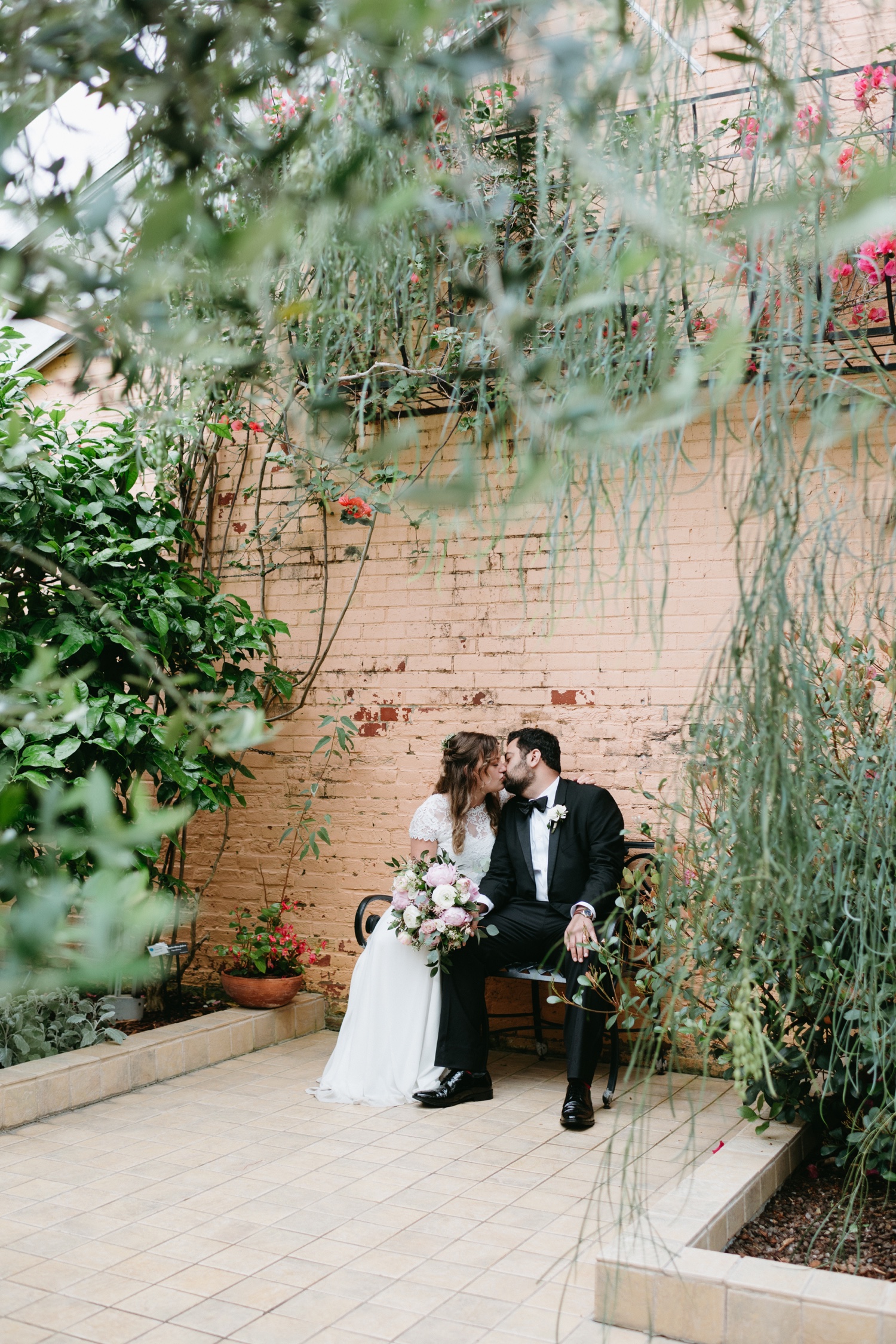bride and groom wedding day kissing sitting on greenhouse bench