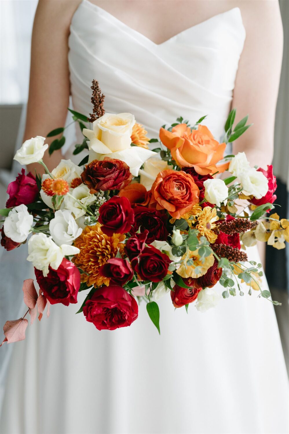 bride holding red and orange warm fall colors bouquet