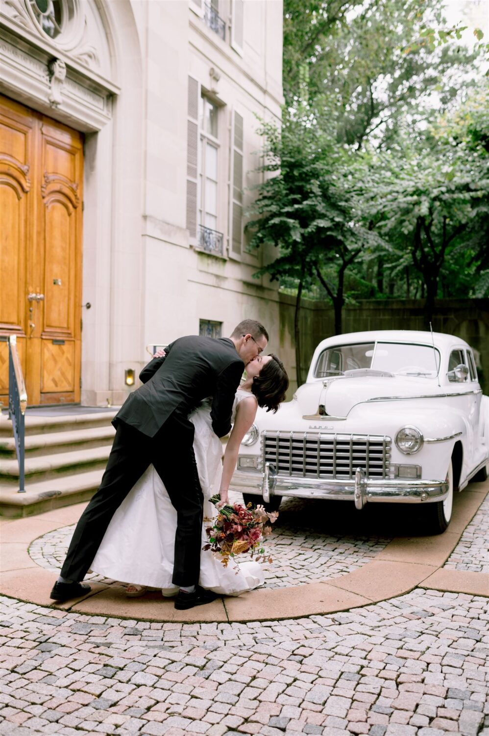 bride and groom dip dance kissing in front of old vintage car city wedding